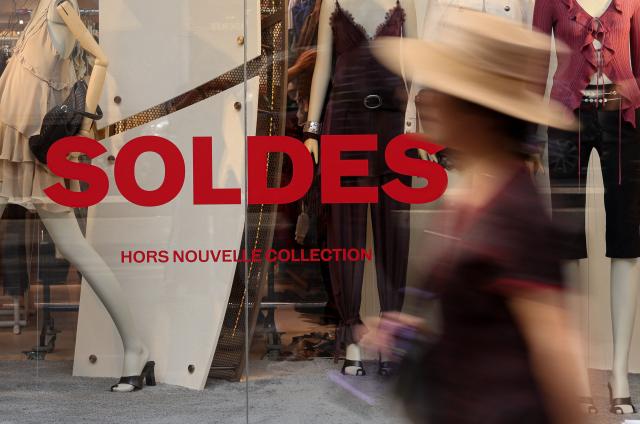 (FILES) A pedestrian walks past the entrance of a clothing store bearing a placard promoting French summer sales on the opening day in Paris on June 24, 2026. France's Prime Minister Sebastien Lecornu has decided to extend the summer sales period, which began on June 24, 2026 in the midst of a heatwave and is causing particular concern for downtown businesses, Matignon said on June 27, 2026, confirming information posted online by La Tribune Dimanche. (Photo by Charlotte SIEMON / AFP)