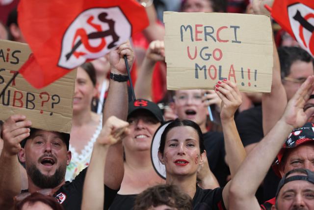A Stade Toulousain's supporter holds a placard reading "thank you Ugo Mola (head coach)" prior to the French Top 14 rugby union final between Stade Toulousain (Toulouse) and Montpellier Hérault Rugby (MHR) at the Stade de France in Saint-Denis, on the outskirst of Paris, on June 27, 2026. (Photo by Kenzo TRIBOUILLARD / AFP)