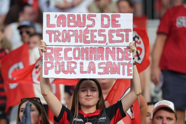 A Stade Toulousain's supporter holds a placard reading "excessive abuse of trophies is recommended for your health" prior to the French Top 14 rugby union final between Stade Toulousain (Toulouse) and Montpellier Hérault Rugby (MHR) at the Stade de France in Saint-Denis, on the outskirst of Paris, on June 27, 2026. (Photo by Kenzo TRIBOUILLARD / AFP)