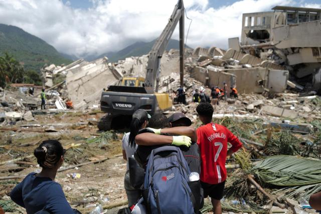 Two people hug as a backhoe loader removes rubble searching for survivors of the twin earthquakes, in Caraballeda, La Guaira State, some 40 km northeast of Caracas, on June 27, 2026. Three days after powerful tremors of magnitude 7.2 and 7.5 killed 1,430 people and left more than 50,000 missing, fury with perceived governmental inaction is mounting -- as is the feeling of helplessness. (Photo by Mauricio VALENZUELA / AFP)