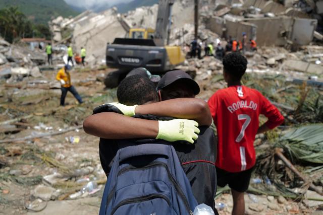 Two people hug as a backhoe loader removes rubble searching for survivors of the twin earthquakes, in Caraballeda, La Guaira State, some 40 km northeast of Caracas, on June 27, 2026. Three days after powerful tremors of magnitude 7.2 and 7.5 killed 1,430 people and left more than 50,000 missing, fury with perceived governmental inaction is mounting -- as is the feeling of helplessness. (Photo by Mauricio VALENZUELA / AFP)