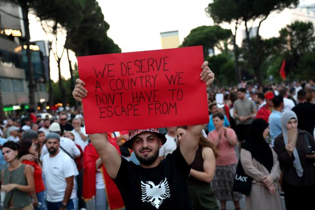 A man demonstrates holding a placard asking for a country people "don't have to escape from" in front of Albania's Prime Minister's office against a planned resort linked to US President's family, in Tirana on June 27, 2026. Since late May, protesters have gathered every evening to oppose the construction of a luxury hotel linked to Trump's daughter Ivanka and her husband Jared Kushner, planned in a nature reserve on the Balkan nation's coast. (Photo by Adnan Beci / AFP)