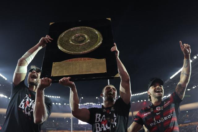 Toulouse's French fly-half Romain Ntamack (R) and Toulouse's French full-back Thomas Ramos (C) celebrate with the "Bouclier de Brennus" trophy after winning the French Top 14 rugby union final against Montpellier Hérault Rugby (MHR) at the Stade de France in Saint-Denis, on the outskirts of Paris, on June 27, 2026. (Photo by Kenzo TRIBOUILLARD / AFP)