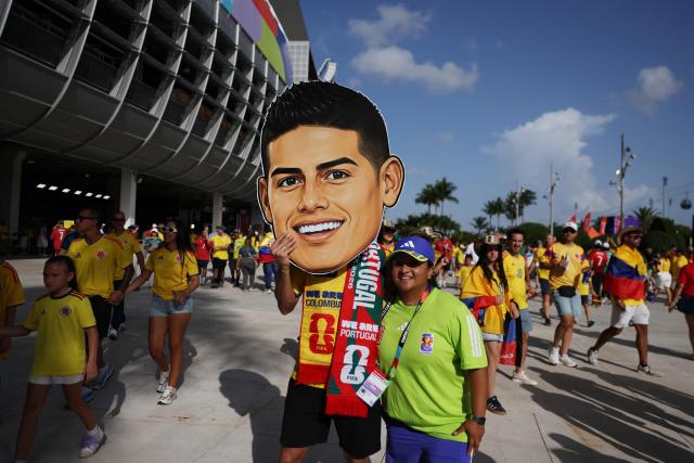 A volunteer poses for a picture with a Colombian fan wearing a mask depicting football player James Rodriguez ahead of the 2026 World Cup Group K football match between Colombia and Portugal at the Miami Stadium in Miami Gardens on June 27, 2026.  (Photo by PATRICIA DE MELO MOREIRA / AFP)
