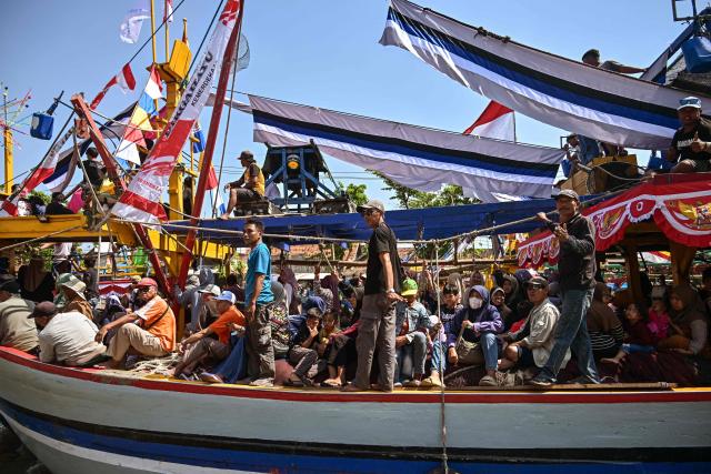 People aboard fishing boats arrive after taking part in the Petik Laut, an annual traditional Javanese thanksgiving ritual during which coastal communities express gratitude for abundant sea harvests, in Pasuruan, East Java province on June 28, 2026. (Photo by Juni KRISWANTO / AFP)