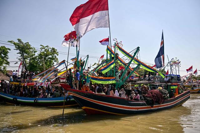 People aboard fishing boats arrive after taking part in the Petik Laut, an annual traditional Javanese thanksgiving ritual during which coastal communities express gratitude for abundant sea harvests, in Pasuruan, East Java province on June 28, 2026. (Photo by Juni KRISWANTO / AFP)