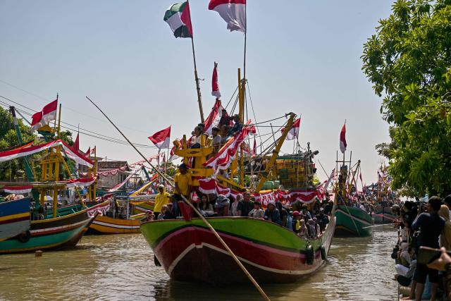 People aboard fishing boats arrive after taking part in the Petik Laut, an annual traditional Javanese thanksgiving ritual during which coastal communities express gratitude for abundant sea harvests, in Pasuruan, East Java province on June 28, 2026. (Photo by Juni KRISWANTO / AFP)