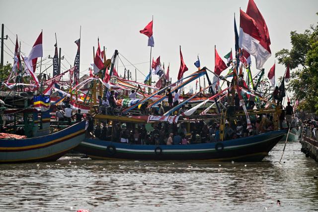 People aboard fishing boats arrive after taking part in the Petik Laut, an annual traditional Javanese thanksgiving ritual during which coastal communities express gratitude for abundant sea harvests, in Pasuruan, East Java province on June 28, 2026. (Photo by Juni KRISWANTO / AFP)