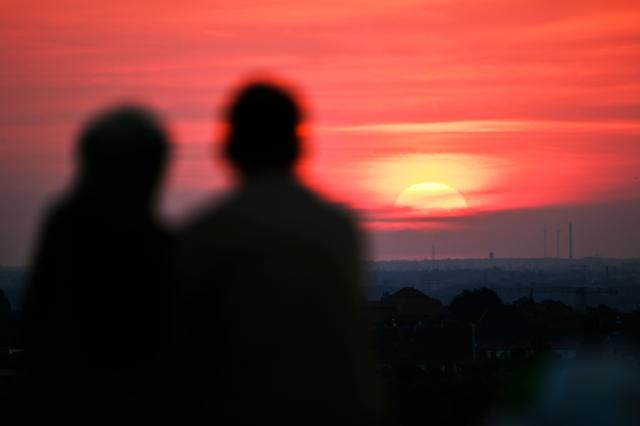 A couple watches the sun going up on early June 28, 2026, over the Drachenberg mountain in Berlin, as the German capital is expected to reach teperatures around 40 degrees Celsius during a heatwave in Europe. Tens of millions are braving a weekend of extreme temperatures in Europe as a deadly heatwave moves eastwards, with some countries announcing rising death tolls and health services warning of saturation. While some mild relief is expected Sunday in western Europe, German forecasters are warning that more temperature records could still be broken over the weekend as eastern countries issue a slew of red alerts for the coming days. (Photo by RALF HIRSCHBERGER / AFP)