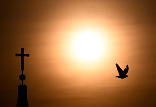 A pigeon fliest past one of the towers of Berlin's landmark next to the rising sun on early June 28, 2026, in Berlin, as the German capital is expected to reach teperatures around 40 degrees Celsius during a heatwave in Europe. Tens of millions are braving a weekend of extreme temperatures in Europe as a deadly heatwave moves eastwards, with some countries announcing rising death tolls and health services warning of saturation. While some mild relief is expected Sunday in western Europe, German forecasters are warning that more temperature records could still be broken over the weekend as eastern countries issue a slew of red alerts for the coming days. (Photo by RALF HIRSCHBERGER / AFP)