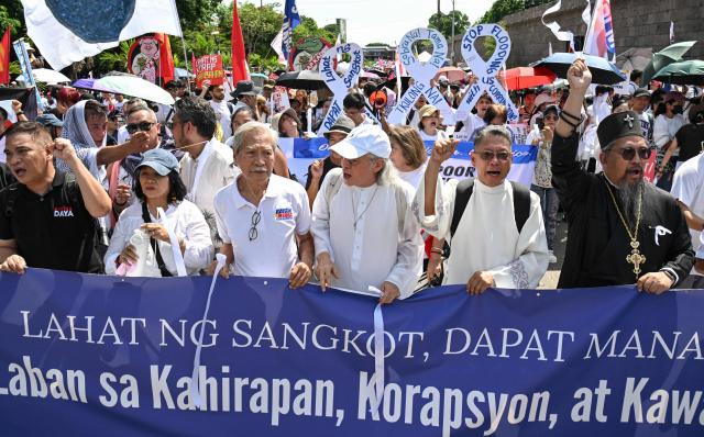 Protesters raise their fists as they march behind a banner during an anti-corruption rally in Manila on June 28, 2026. Hundreds of protesters including members of religious groups marched to the people power monument demanding accountability over a multi-billion-dollar infrastructure scandal that has seen scores of officials, lawmakers and construction firm owners accused of corruption. (Photo by Ted ALJIBE / AFP)