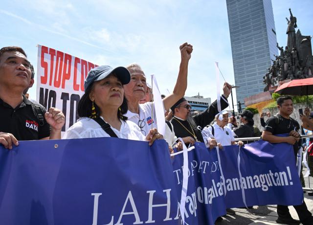 Protesters raise their fists as they march behind a banner past the People Power monument (R) during an anti-corruption rally in Manila on June 28, 2026. Hundreds of protesters including members of religious groups marched to the people power monument demanding accountability over a multi-billion-dollar infrastructure scandal that has seen scores of officials, lawmakers and construction firm owners accused of corruption. (Photo by Ted ALJIBE / AFP)