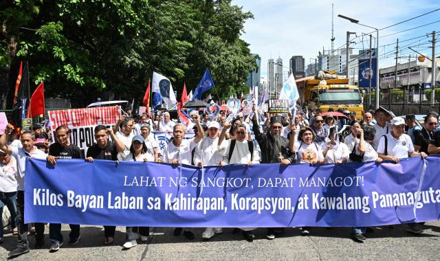 Protesters raise their fists as they march behind a banner during an anti-corruption rally in Manila on June 28, 2026. Hundreds of protesters including members of religious groups marched to the people power monument demanding accountability over a multi-billion-dollar infrastructure scandal that has seen scores of officials, lawmakers and construction firm owners accused of corruption. (Photo by Ted ALJIBE / AFP)