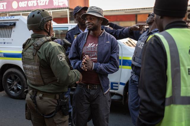 Private security officers detain a pedestrian as he pleads with them to be let go during a joint patrol in the Johannesburg CBD on June 28, 2026. The operation, conducted alongside members of the South African Police Service (SAPS) (unseen) forms part of Operation Shanela, a policing initiative targeting the inner city. The coordinated effort sees SAPS working in closer operational alignment with private security firms, such as Professional Protection Security (PPS). Focus areas include crime prevention, immigration compliance checks, and on-the-ground intelligence gathering. (Photo by EMMANUEL CROSET / AFP)