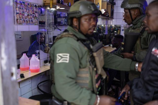 Private security officers detain a barber as his client looks on during a joint patrol in the Johannesburg CBD on June 28, 2026. The operation, conducted alongside members of the South African Police Service (SAPS) (unseen) forms part of Operation Shanela, a policing initiative targeting the inner city. The coordinated effort sees SAPS working in closer operational alignment with private security firms, such as Professional Protection Security (PPS). Focus areas include crime prevention, immigration compliance checks, and on-the-ground intelligence gathering. (Photo by EMMANUEL CROSET / AFP)