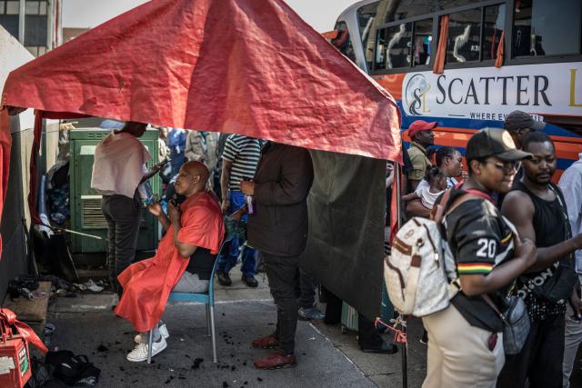 TOPSHOT - A man trims his beard at a roadside barber shop as undocumented migrants, mostly Zimbabwean, Malawians and Mozambicans, gather at the Cartwright Old Taxi Rank before boarding a bus heading to Zimbabwe in Durban, on June 28, 2026. South Africans President Cyril Ramaphosa vowed on Thursday to crush any attempts to destabilise the nation during planned anti-immigrant marches next week, amid a wave of xenophobia. Citizen-led groups have set Tuesday 30 as a deadline for undocumented foreigners to leave and called for nationwide marches against illegal immigration, marking a crescendo in months of protests that have at times turned violent. (Photo by MARCO LONGARI / AFP)