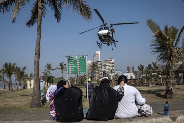 TOPSHOT - A family sits on a bench as a South African Police Service (SAPS) helicopter takes off in Durban, on June 28, 2026. Members of the South African police Service (SAPS) displayed their readiness ahead of the June 30th deadline on undocumented foreigners imposed by anti immigration groups. South Africans President Cyril Ramaphosa vowed on Thursday to crush any attempts to destabilise the nation during planned anti-immigrant marches next week, amid a wave of xenophobia. Citizen-led groups have set Tuesday 30 as a deadline for undocumented foreigners to leave and called for nationwide marches against illegal immigration, marking a crescendo in months of protests that have at times turned violent. (Photo by MARCO LONGARI / AFP)