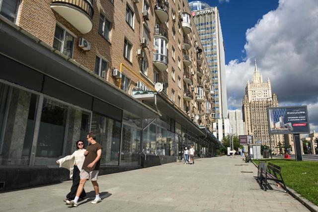 People walk past the empty display windows of closed shops with the Russian Foreign Ministry building in the background in Moscow on June 28, 2026. (Photo by Igor IVANKO / AFP)