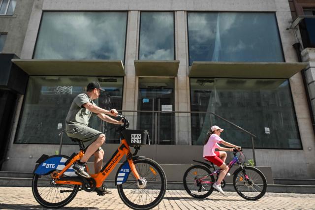 People cycle past the empty display windows of a closed shop in Moscow on June 28, 2026. (Photo by Igor IVANKO / AFP)