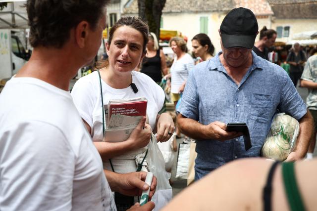 National secretary of French left-wing The Ecologistes party Marine Tondelier (C) distributes flyers as she speaks with customers at the market in Issigeac, southwestern France on June 28, 2026, as part of a tour of France in an electric van. (Photo by ROMAIN PERROCHEAU / AFP)