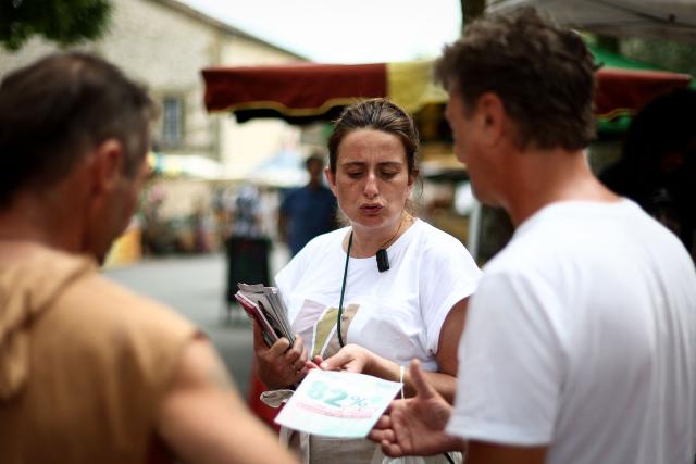 National secretary of French left-wing The Ecologistes party Marine Tondelier (C) distributes flyers as she speaks with customers at the market in Issigeac, southwestern France on June 28, 2026, as part of a tour of France in an electric van. (Photo by ROMAIN PERROCHEAU / AFP)