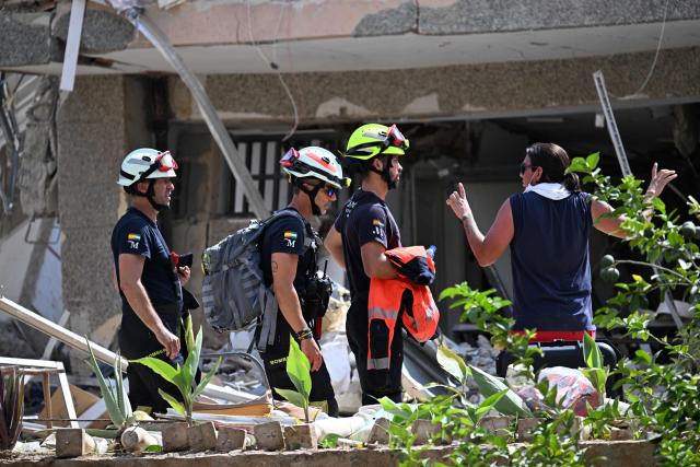 Spanish rescuers talk with a person in front of a collapsed building in Catia La Mar, La Guaira state, Venezuela, on June 28, 2026, following earthquakes. Thousands of rescuers, relatives and volunteers dig day and night through mounds of concrete to find survivors of the earthquakes that struck Venezuela more than three days ago, leaving nearly 1,500 dead and tens of thousands missing. (Photo by Juan BARRETO / AFP)