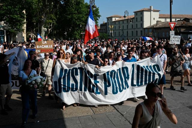 People hold a national flag and a banner reading "Justice for Louis" during a rally in the memory of Louis, a 17-year-old boy who died after being beaten up by five young people during an ambush, in Narbonne, southern France, on June 28, 2026. France's Interior Minister condemned in an interview the “exploitation of the case by the far right” involving the 17-year-old boy and said that five young men, aged between 16 and 20, have been charged with murder in connection with this case. (Photo by Matthieu RONDEL / AFP)