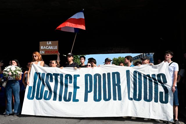 People hold a national flag and a banner reading "Justice for Louis" during a rally in the memory of Louis, a 17-year-old boy who died after being beaten up by five young people during an ambush, in Narbonne, southern France, on June 28, 2026. France's Interior Minister condemned in an interview the “exploitation of the case by the far right” involving the 17-year-old boy and said that five young men, aged between 16 and 20, have been charged with murder in connection with this case. (Photo by Matthieu RONDEL / AFP)