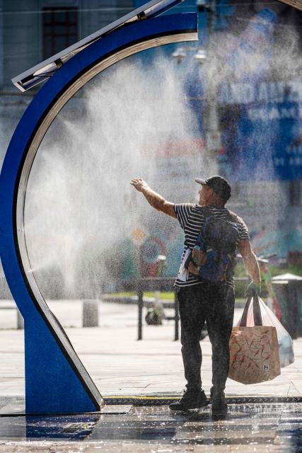 A man cools of while walking through a water sprayer installed in central Bucharest, on June 28, 2026. The Romanian National Meteorological Administration (ANM) has issued a critical red heatwave warning across the country, with localized temperatures in Bucharest soaring up to 39°C (102°F). (Photo by Mihai Barbu / AFP)