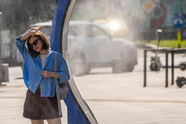 A woman cools off while walking through a water sprayer installed in central Bucharest, on June 28, 2026. The Romanian National Meteorological Administration (ANM) has issued a critical red heatwave warning across the country, with localized temperatures in Bucharest soaring up to 39°C (102°F). (Photo by Mihai Barbu / AFP)