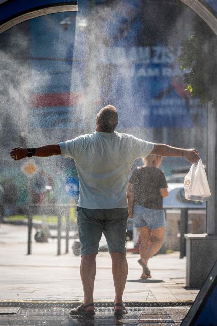 A man cools of while walking through a water sprayer installed in central Bucharest, on June 28, 2026. The Romanian National Meteorological Administration (ANM) has issued a critical red heatwave warning across the country, with localized temperatures in Bucharest soaring up to 39°C (102°F). (Photo by Mihai Barbu / AFP)