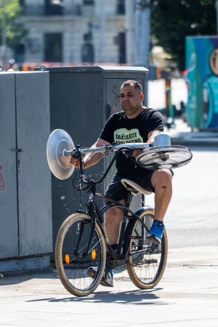 A man rides a bicycle carrying an electric fan in central Bucharest, on June 28, 2026. The Romanian National Meteorological Administration (ANM) has issued a critical red heatwave warning across the country, with localized temperatures in Bucharest soaring up to 39°C (102°F). (Photo by Mihai Barbu / AFP)