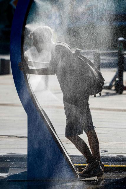 A man cools of while walking through a water sprayer installed in central Bucharest, on June 28, 2026. The Romanian National Meteorological Administration (ANM) has issued a critical red heatwave warning across the country, with localized temperatures in Bucharest soaring up to 39°C (102°F). (Photo by Mihai Barbu / AFP)