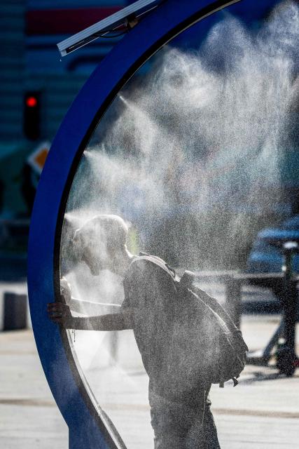 A man cools of while walking through a water sprayer installed in central Bucharest, on June 28, 2026. The Romanian National Meteorological Administration (ANM) has issued a critical red heatwave warning across the country, with localized temperatures in Bucharest soaring up to 39°C (102°F). (Photo by Mihai Barbu / AFP)