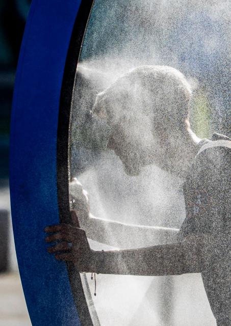 A man cools off while walking through a water sprayer installed in central Bucharest, on June 28, 2026. The Romanian National Meteorological Administration (ANM) has issued a critical red heatwave warning across the country, with localized temperatures in Bucharest soaring up to 39°C (102°F). (Photo by Mihai Barbu / AFP) / ALTERNATIVE CROP