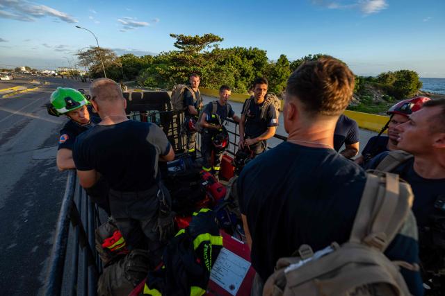 Members of the French Civil Security Training and Intervention Regiment (UIISC 7) ride in the back of a truck through an area affected by building collapses in La Guaira state, Venezuela, on June 28, 2026, following earthquakes. Thousands of rescuers, relatives and volunteers dig day and night through mounds of concrete to find survivors of the earthquakes that struck Venezuela more than three days ago, leaving nearly 1,500 dead and tens of thousands missing. (Photo by Miguel MEDINA / POOL / AFP)