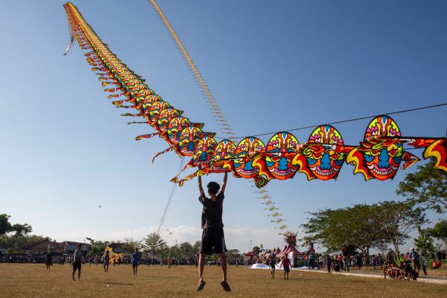 A participant is briefly lifted into the air as a giant dragon train kite catches the wind during a kite festival in Bantul, Yogyakarta, on June 28, 2026. (Photo by DEVI RAHMAN / AFP)
