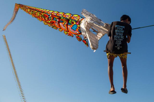 A participant is briefly lifted into the air as a giant dragon train kite catches the wind during a kite festival in Bantul, Yogyakarta, on June 28, 2026. (Photo by DEVI RAHMAN / AFP)