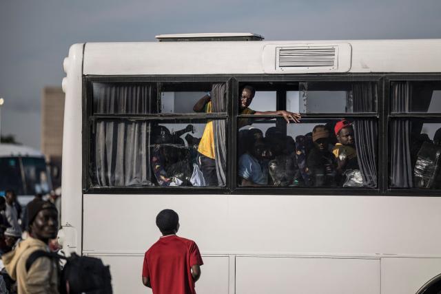 An undocumented migrant gestures from a bus to others still present at the Durban Drive In in Durban, on June 29, 2026 before the camp will shut down and the operation will be transferred to the border with Zimbabwe. South Africans President Cyril Ramaphosa vowed on June 25 to crush any attempts to destabilise the nation during planned anti-immigrant marches next week, amid a wave of xenophobia. Citizen-led groups have set Tuesday 30 as a deadline for undocumented foreigners to leave and called for nationwide marches against illegal immigration, marking a crescendo in months of protests that have at times turned violent. (Photo by MARCO LONGARI / AFP)