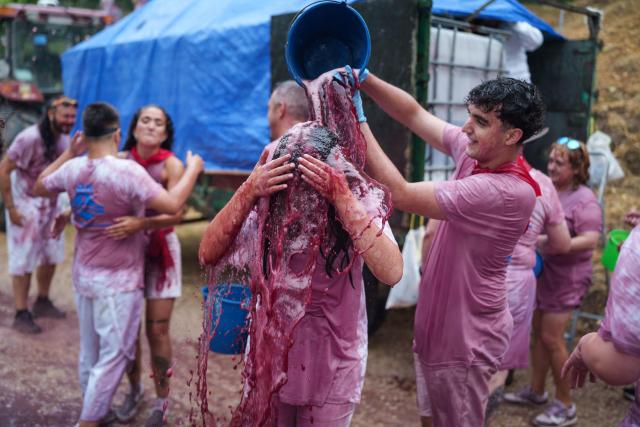 A reveller pours a bucket full of red wine on a participant during the"Batalla del Vino" (Battle of Wine) in Haro, in the wine producing region of La Rioja, on June 29, 2026. Every year thousands of locals and tourists climb a mountain in the northern Spanish wine producing region of La Rioja to celebrate St. Peter's day by covering each other in red wine using water pistols, back mounted spraying devices, buckets which are randomly poured on heads and into any other available container. (Photo by CESAR MANSO / AFP)