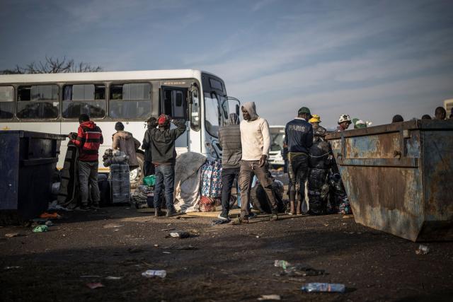 Undocumented migrants line up near a bus at the Durban Drive In in Durban, on June 29, 2026 preparing to leave before the shutting down of the camp and the operation will be transferred to the border with Zimbabwe. South Africans President Cyril Ramaphosa vowed on June 25 to crush any attempts to destabilise the nation during planned anti-immigrant marches next week, amid a wave of xenophobia. Citizen-led groups have set Tuesday 30 as a deadline for undocumented foreigners to leave and called for nationwide marches against illegal immigration, marking a crescendo in months of protests that have at times turned violent. (Photo by MARCO LONGARI / AFP)