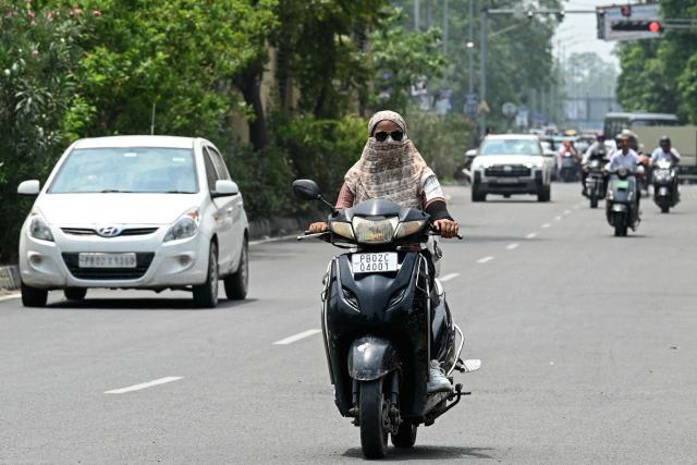 A commuter with her face covered in cloth rides along a street on a hot afternoon in Amritsar on June 29, 2026. (Photo by Narinder NANU / AFP)