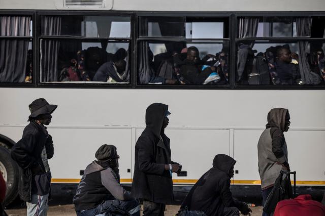 TOPSHOT - Undocumented migrants line up near a bus carrying others outside the Durban Drive In in Durban, on June 29, 2026. Authorities refused to take in more undocumented migrants after the operation in Durban was shut down and transferred to the border with Zimbabwe. Migrants will have to make their way to the border paying from their pockets. (Photo by MARCO LONGARI / AFP)
