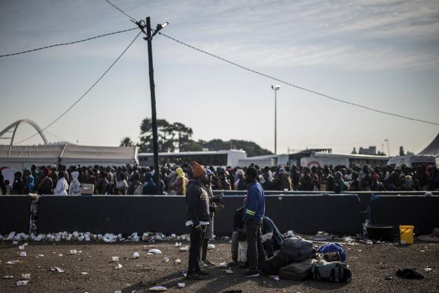 Undocumented migrants gather near their belongings as other line up next to busses at the Durban Drive In in Durban, on June 29, 2026 preparing to leave before the shut down of the camp and the operation will be transferred to the border with Zimbabwe. South Africans President Cyril Ramaphosa vowed on June 25 to crush any attempts to destabilise the nation during planned anti-immigrant marches next week, amid a wave of xenophobia. Citizen-led groups have set Tuesday 30 as a deadline for undocumented foreigners to leave and called for nationwide marches against illegal immigration, marking a crescendo in months of protests that have at times turned violent. (Photo by MARCO LONGARI / AFP)