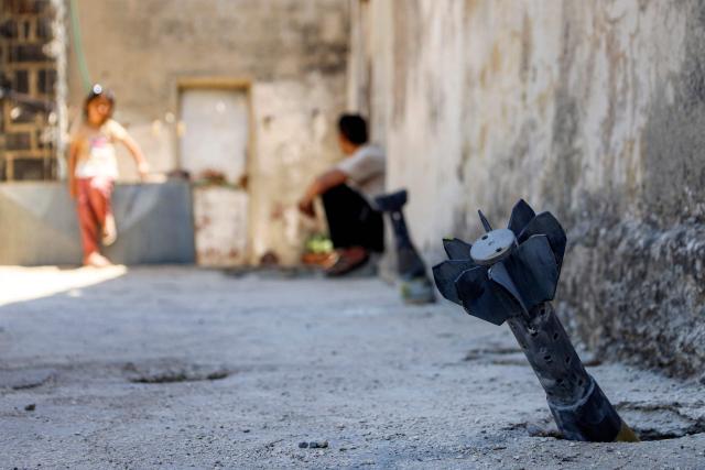 A man speaks with a child while sitting near an unexploded artillery shell that fell during reported overnight Israeli bombardment that hit the village of Abidin in Syria's southwestern Daraa province, close to the Golan Heights, on June 29, 2026. Syria's foreign ministry condemned on June 29 Israeli incursions and shelling in the south of the country, a day after an escalation in the village in Daraa province forced its residents to temporarily flee, according to local officials. (Photo by Sam HARIRI / AFP)