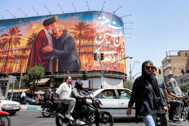 People cross a street past a billboard depicting Iran's slain supreme leader Ali Khamenei kissing the slain Islamic revolutionary guards commander Qasem Soleimani near the shrine of Imam Hussein Iraq's holy city of Karbala, displayed on the facade of a building in Tehran on June 29, 2026. Iran had on June 23 announced three days of public holidays, from July 4 to 6, in the capital Tehran for late supreme leader Ayatollah Ali Khamenei's funeral ceremonies, state television reported. He will finally be laid to rest on July 9 in the northeastern holy city of Mashhad, his birthplace. Khamenei was killed in a strike on the first day of the US-Israeli war against the Iran on February 28. (Photo by AFP) / 