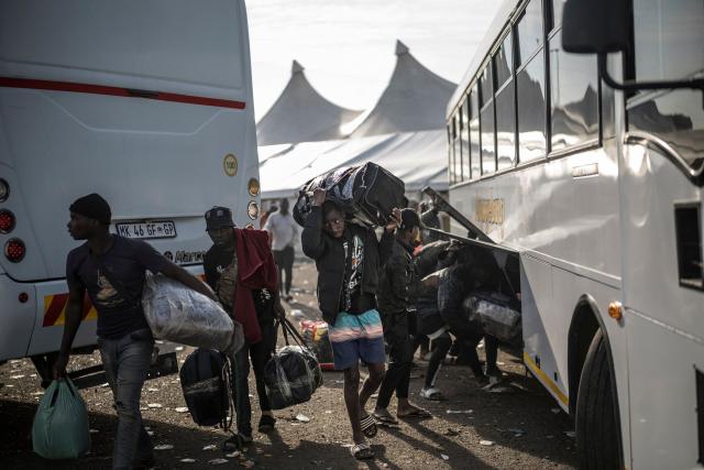 Undocumented migrants carry their belongings towards busses leaving from the Durban Drive In in Durban, on June 29, 2026 before the camp will shut down and the operation will be transferred to the border with Zimbabwe. South Africans President Cyril Ramaphosa vowed on June 25 to crush any attempts to destabilise the nation during planned anti-immigrant marches next week, amid a wave of xenophobia. Citizen-led groups have set Tuesday 30 as a deadline for undocumented foreigners to leave and called for nationwide marches against illegal immigration, marking a crescendo in months of protests that have at times turned violent. (Photo by MARCO LONGARI / AFP)