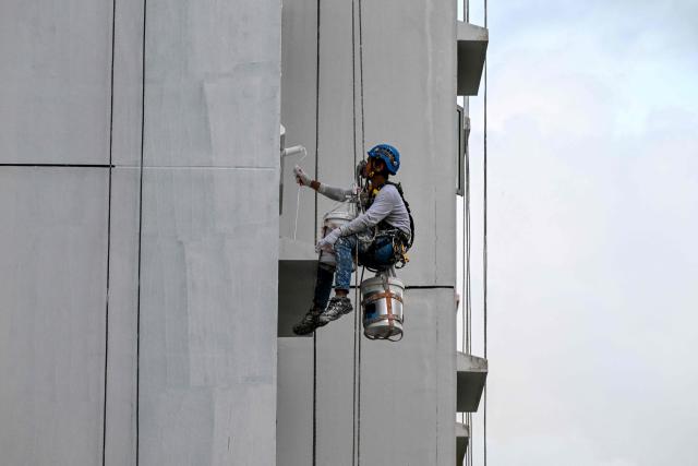 A worker supported on safety ropes paints the facade of an apartment building in Singapore on June 29, 2026. (Photo by Roslan RAHMAN / AFP)