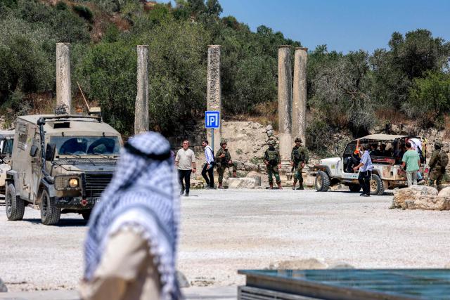 A Palestinian man looks on near Israeli settlers gathering during an official visit by a group of foreign diplomats accredited by the Palestinian Authority at the archaeological site of Sebastia, north of Nablus in the occupied West Bank, on June 29, 2026. (Photo by Jaafar ASHTIYEH / AFP)