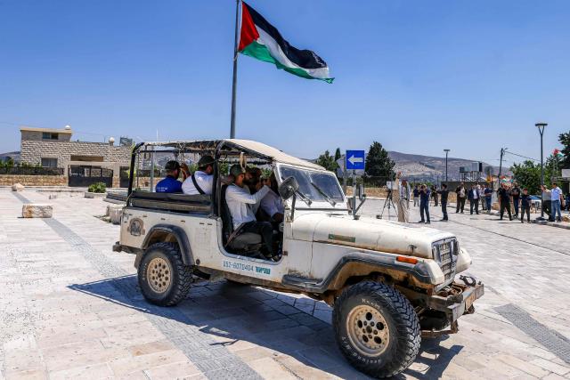Israeli settlers sit in a four-wheel drive vehicle parked near a group of foreign diplomats accredited by the Palestinian Authority touring during an official visit at the archaeological site of Sebastia, north of Nablus in the occupied West Bank, on June 29, 2026. (Photo by JAAFAR ASHTIYEH / AFP)